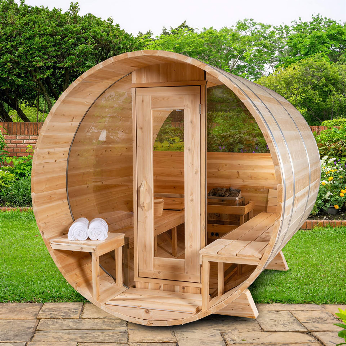 Round wood barrel sauna with a glass front wall and door, featuring interior benches and a heater in a garden setting.