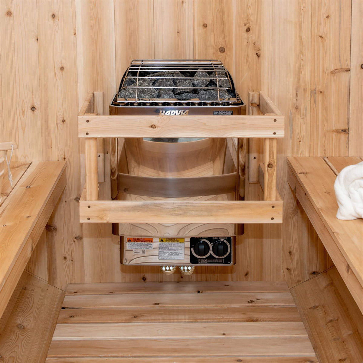 Silver metal Harvia KIP electric sauna heater with stones and a wood guardrail mounted on a light wood wall.