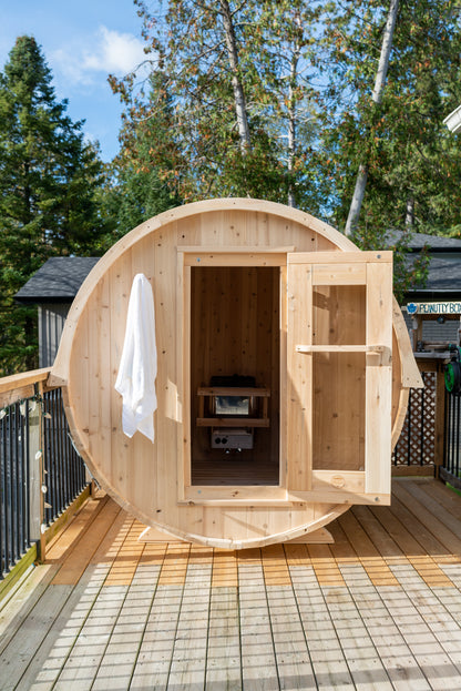 Wooden barrel-shaped sauna on a wooden deck with trees in the background