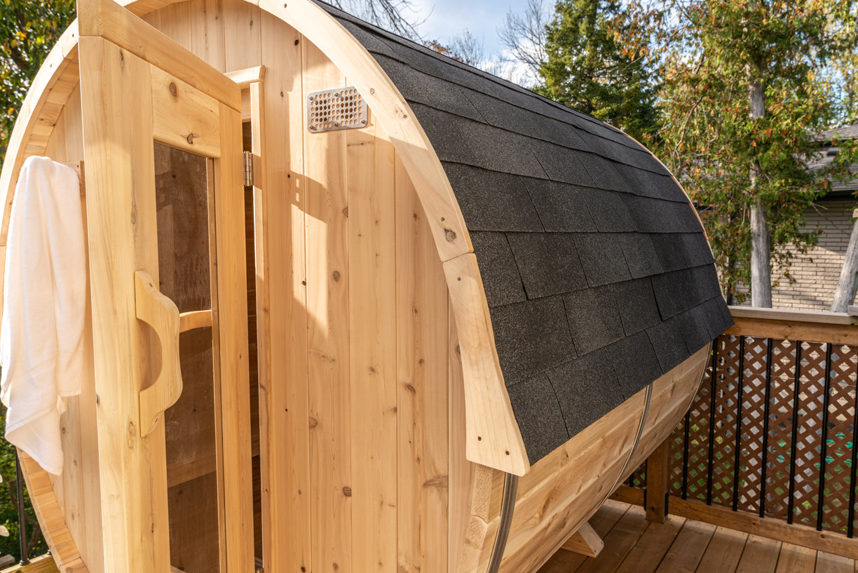 Wooden barrel-shaped sauna with a shingled roof on a wooden deck.