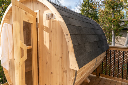 Wooden barrel-shaped sauna with a shingled roof on a wooden deck.