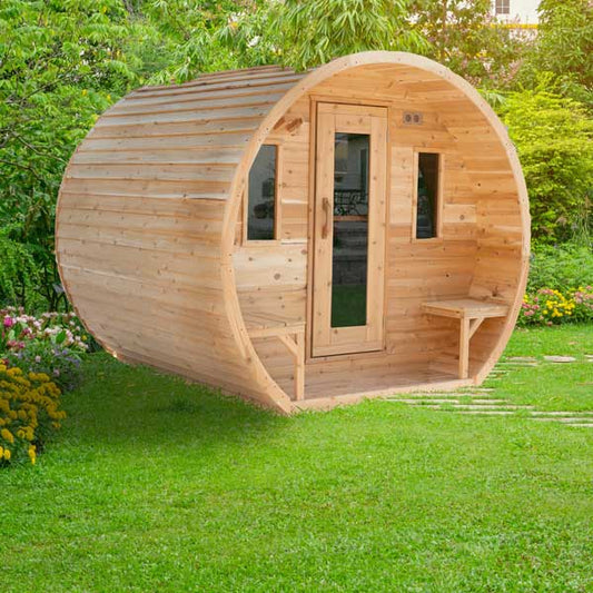 Wooden barrel like sauna on a grassy area with greenery in the background