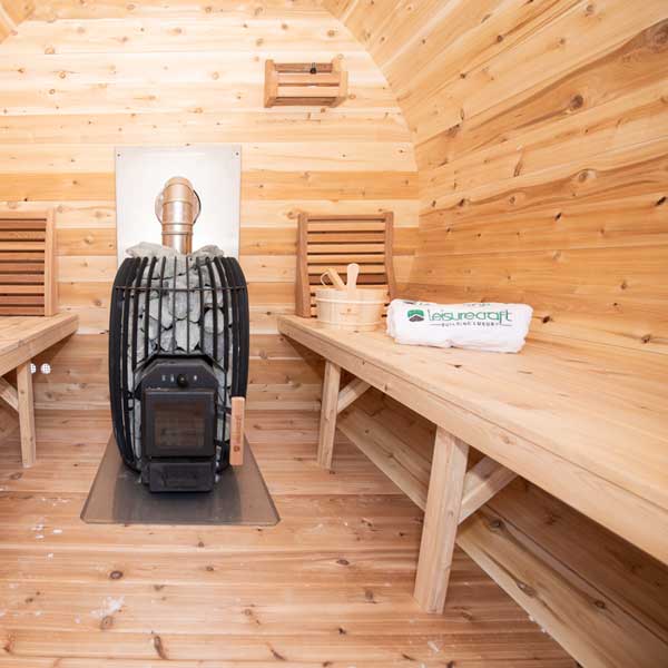 Wood-fired sauna heater in a wooden sauna room with benches and a Leisurecraft logo.