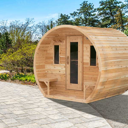 Wooden barrel-shaped sauna on a paved area with trees in the background