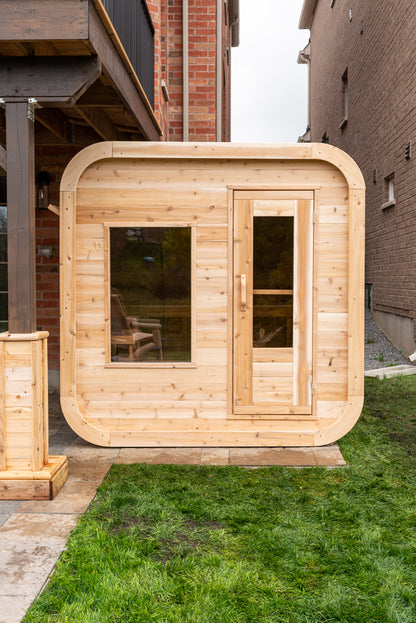 Wooden outdoor sauna with glass door and large window sitting next to a brick building.