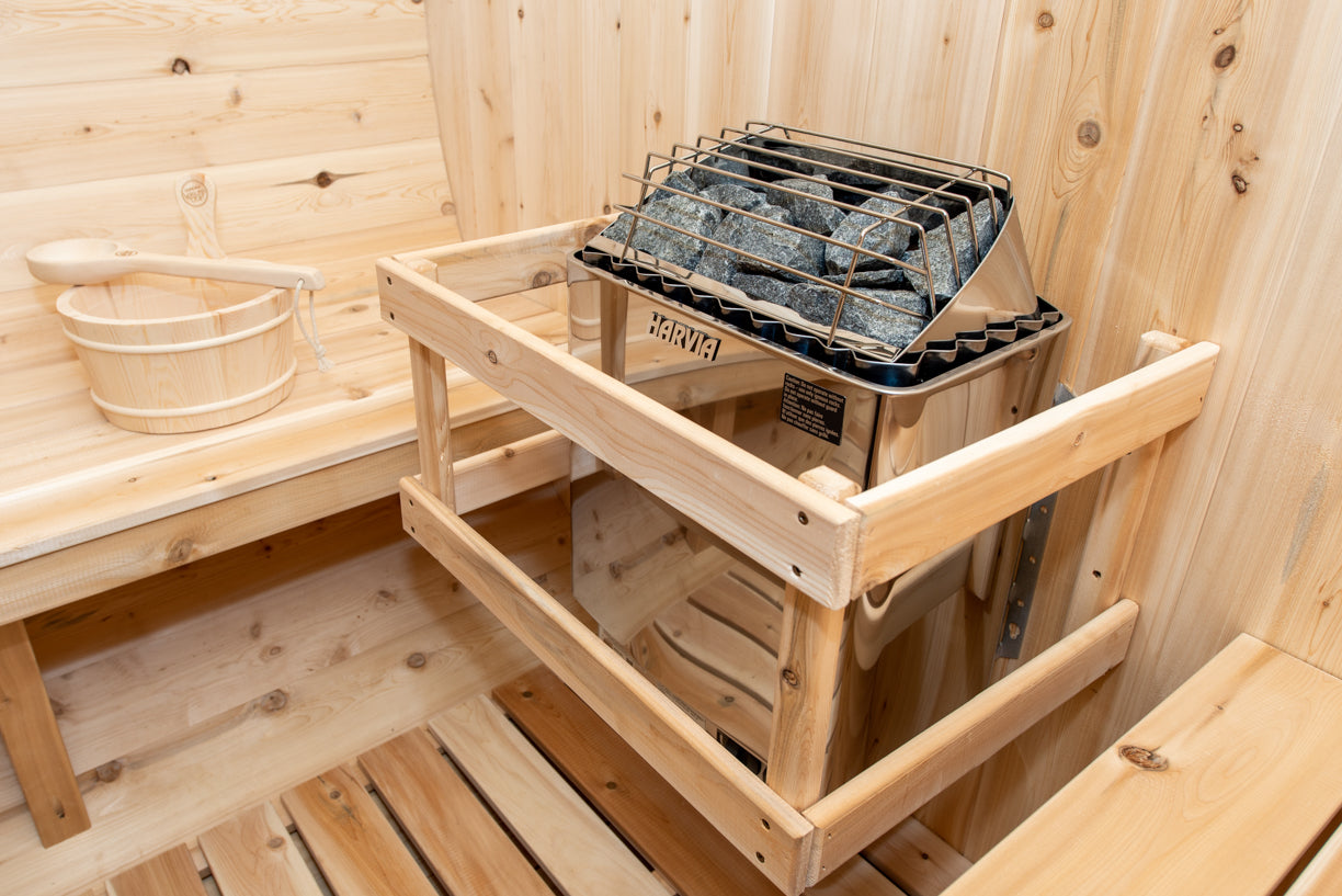 Wooden sauna interior with a metal basket and stones on a shelf.