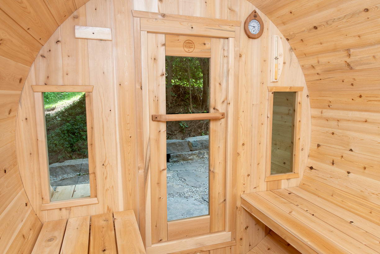 Wooden sauna with arched windows and a bench, surrounded by nature.