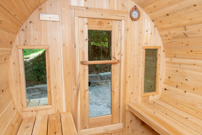 Wooden sauna with arched windows and a bench, surrounded by nature.
