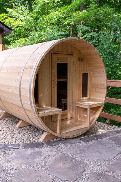 Wooden barrel-shaped sauna in a natural setting with trees in the background.