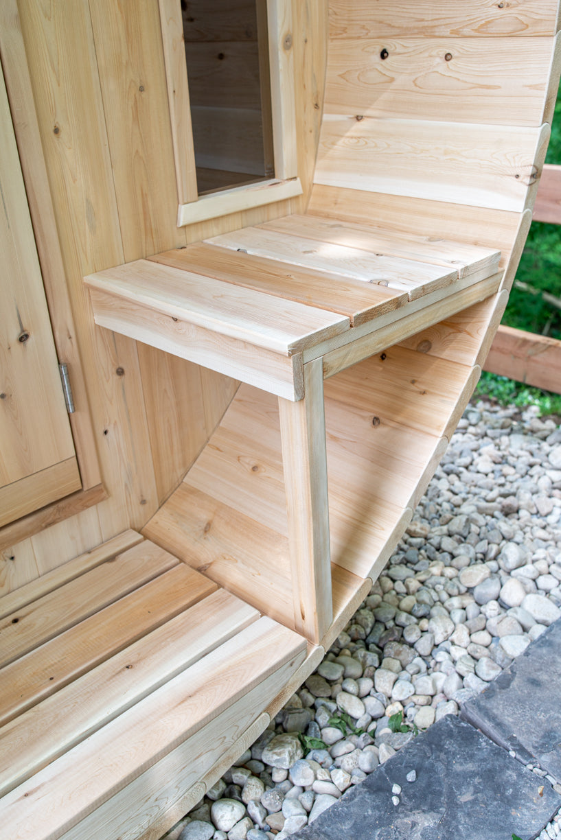 Wooden outdoor barrel sauna close up of bench on porch on a gravel surface.