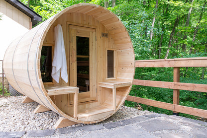 Wooden barrel sauna on a stone platform with greenery in the background