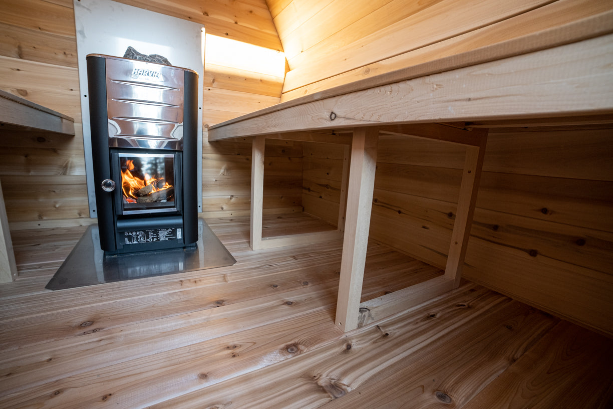 Wood-burning stove in a wooden cabin with a bench.
