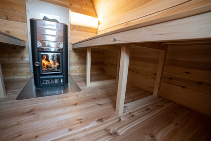 Wood-burning stove in a wooden cabin with a bench.