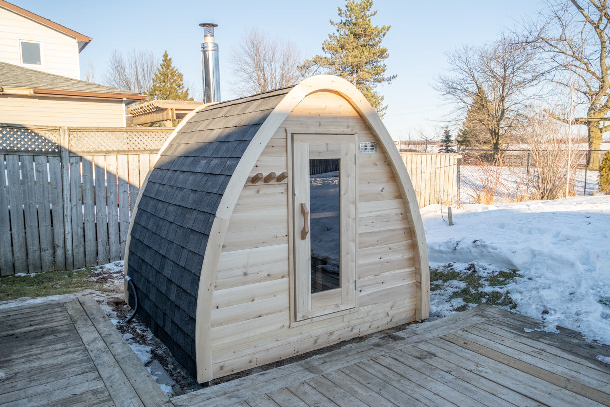 CT MiniPOD Woodburning Sauna by Leisurecraft beside a wooden deck with snow and trees in the background
