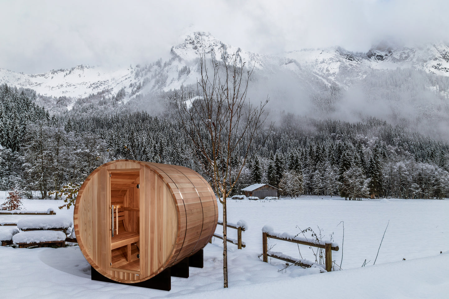 Golden Designs "Arosa" 4-Person Barrel Sauna in snow covered yard with rugged mountains in the background