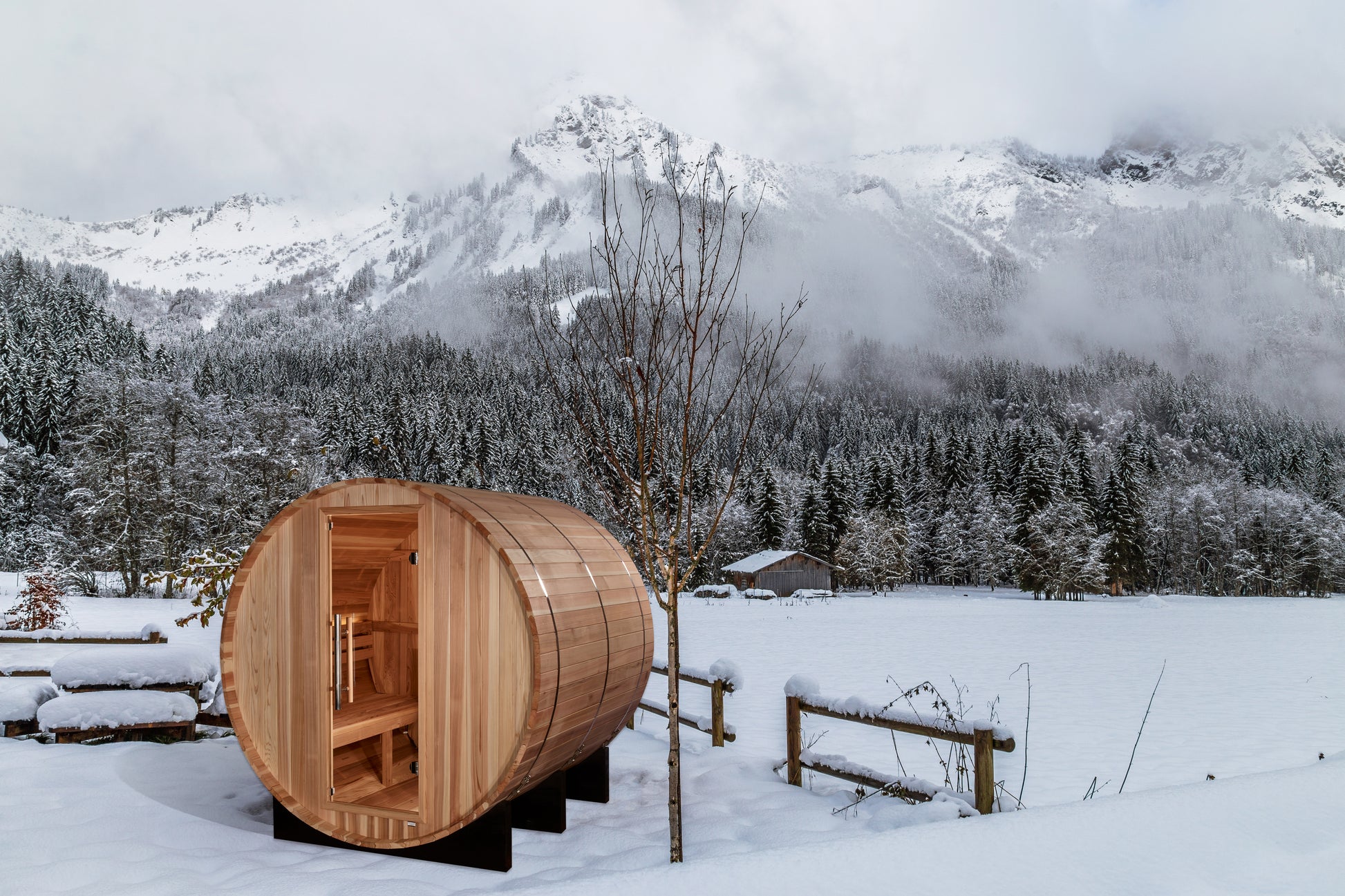 Golden Designs "Arosa" 4-Person Barrel Sauna in snow covered yard with rugged mountains in the background