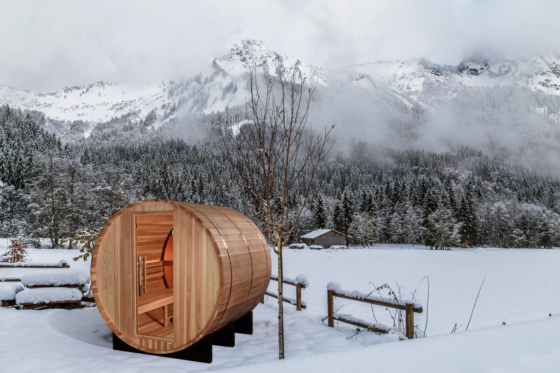 Golden Designs "Zurich" 4 Person Barrel sauna pictured in a yard with rugged snow covered mountains in the background