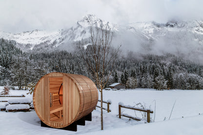 Golden Designs "Zurich" 4 Person Barrel sauna pictured in a yard with rugged snow covered mountains in the background