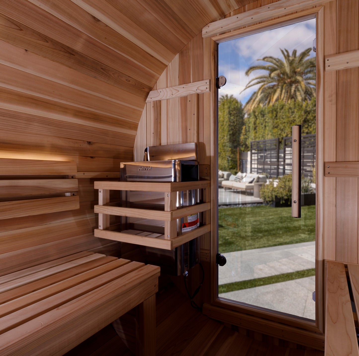 Golden Designs "Zurich" 4 Person Barrel sauna interior pictured showing the electric heater and bench seating and solid glass door. 