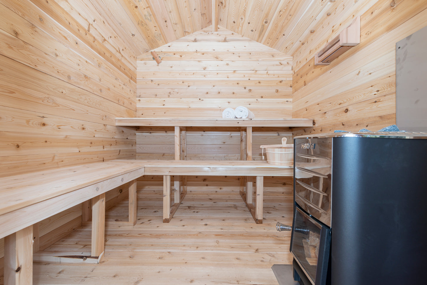 Wooden sauna interior with benches, table, and a black metal sauna heater.