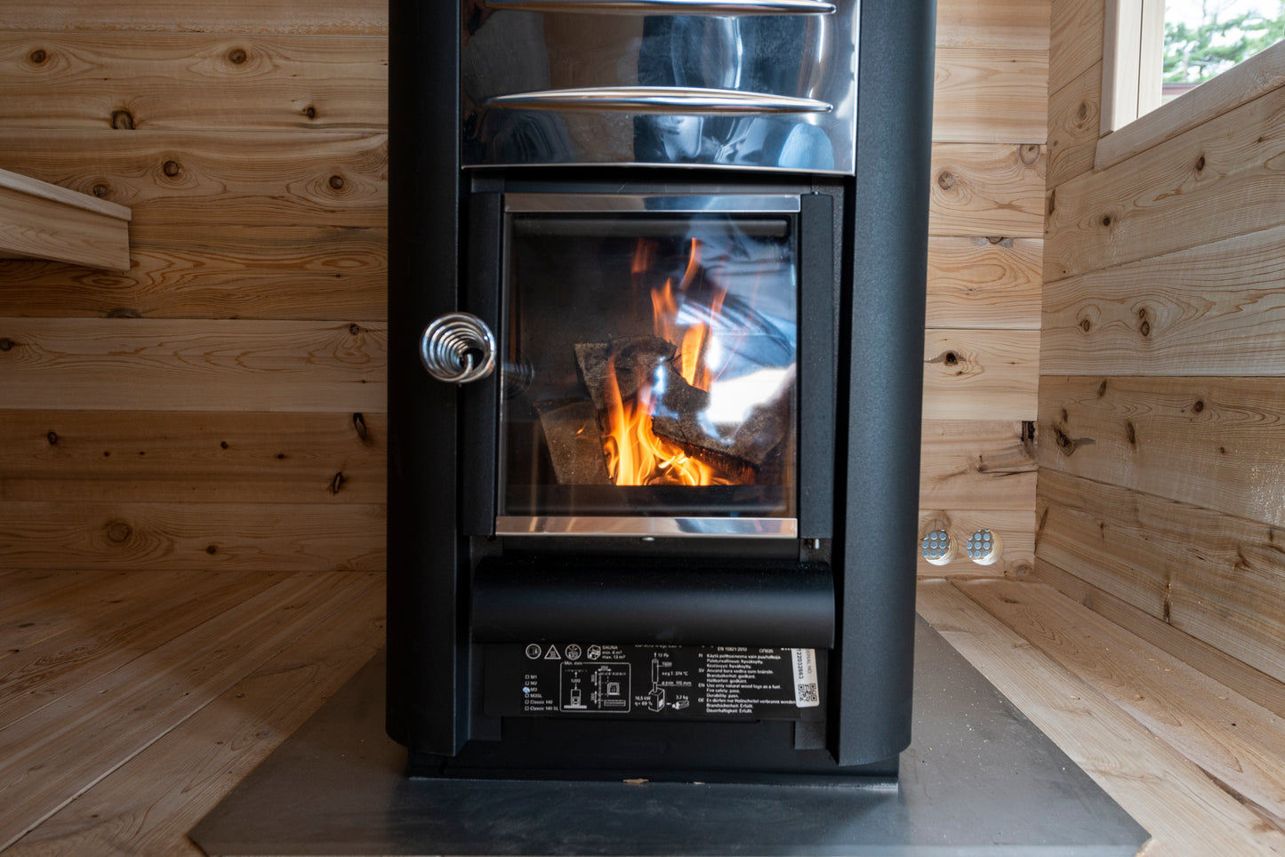 Wood-burning stove in a wooden cabin with visible flames.