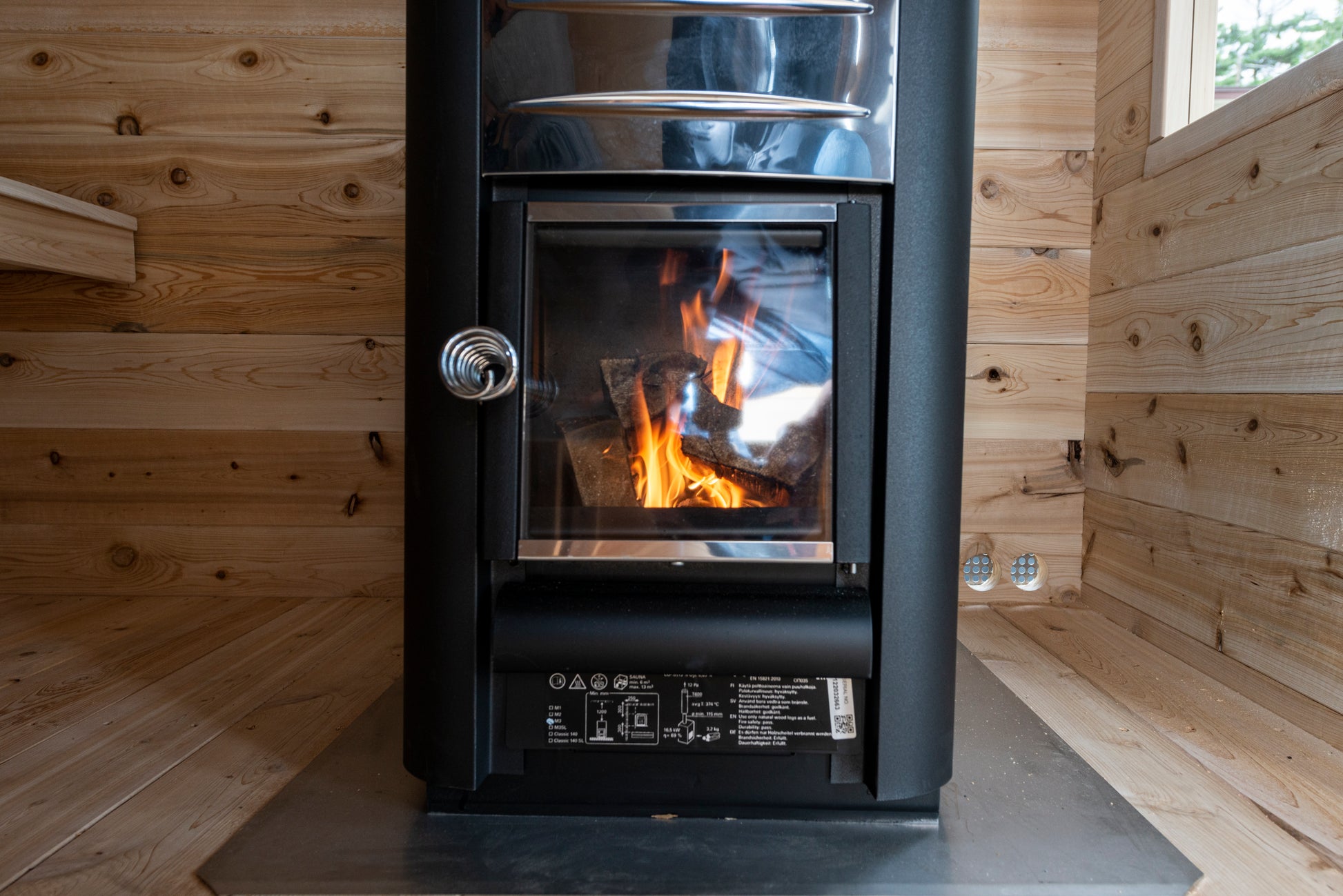 Wood-burning stove in a wooden cabin with visible flames.