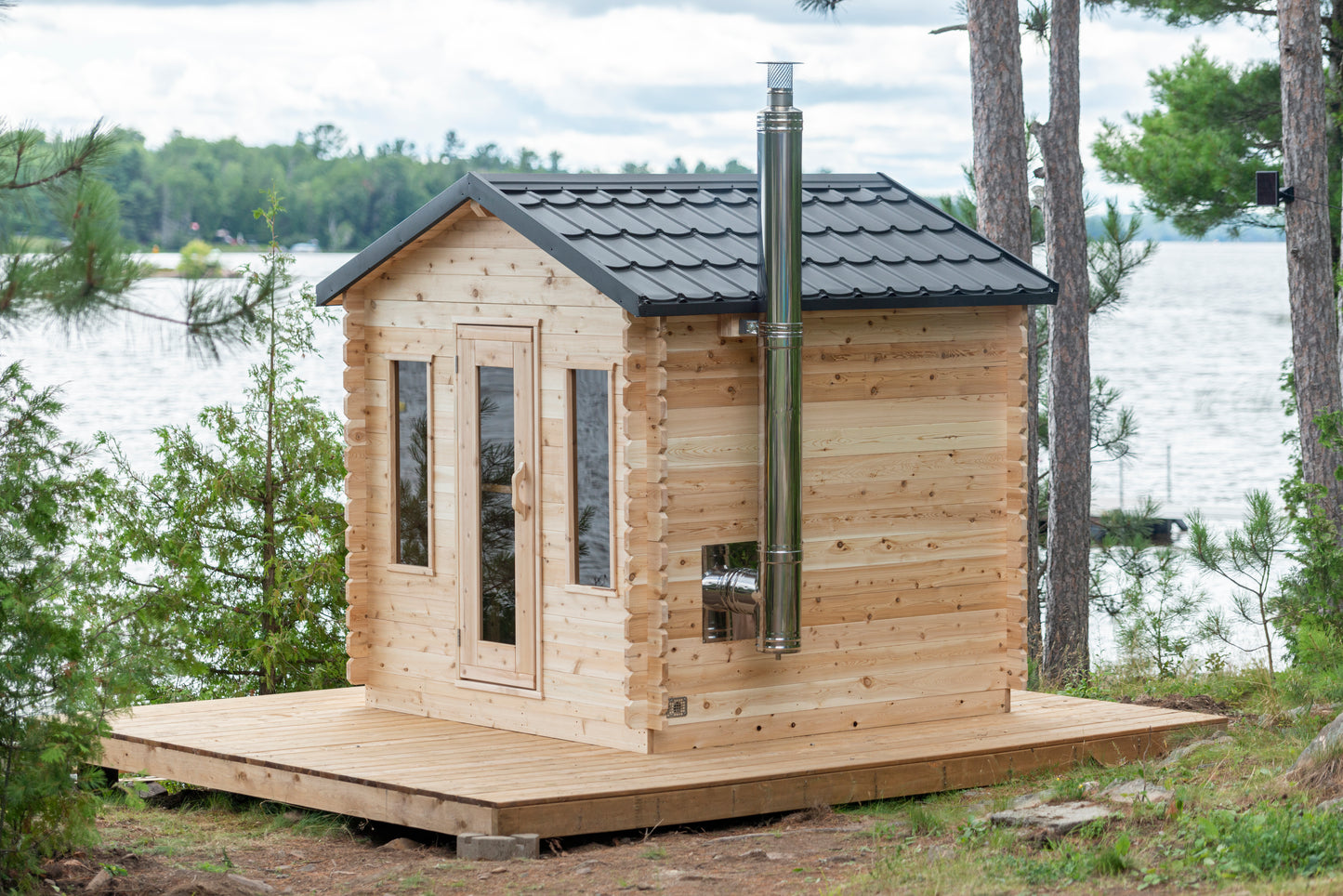 Wooden cabin with a black roof on a platform surrounded by trees and water