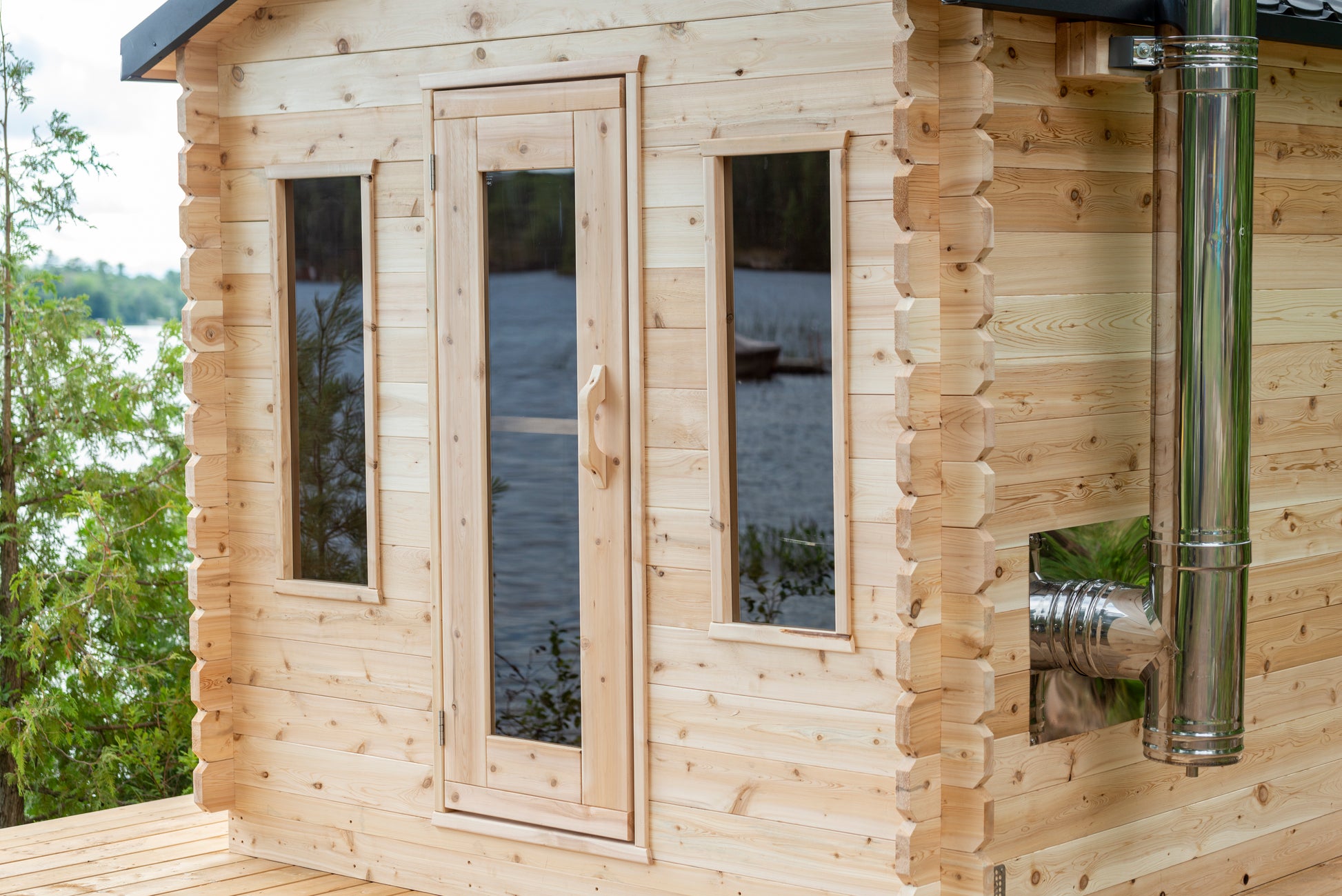 Wooden cabin with windows overlooking a body of water and trees.