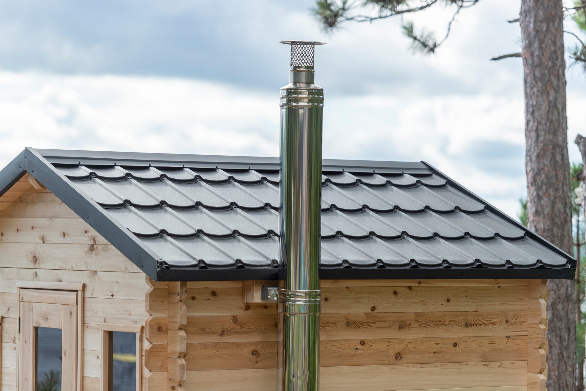 Wooden cabin with a metal chimney pipe against a cloudy sky.