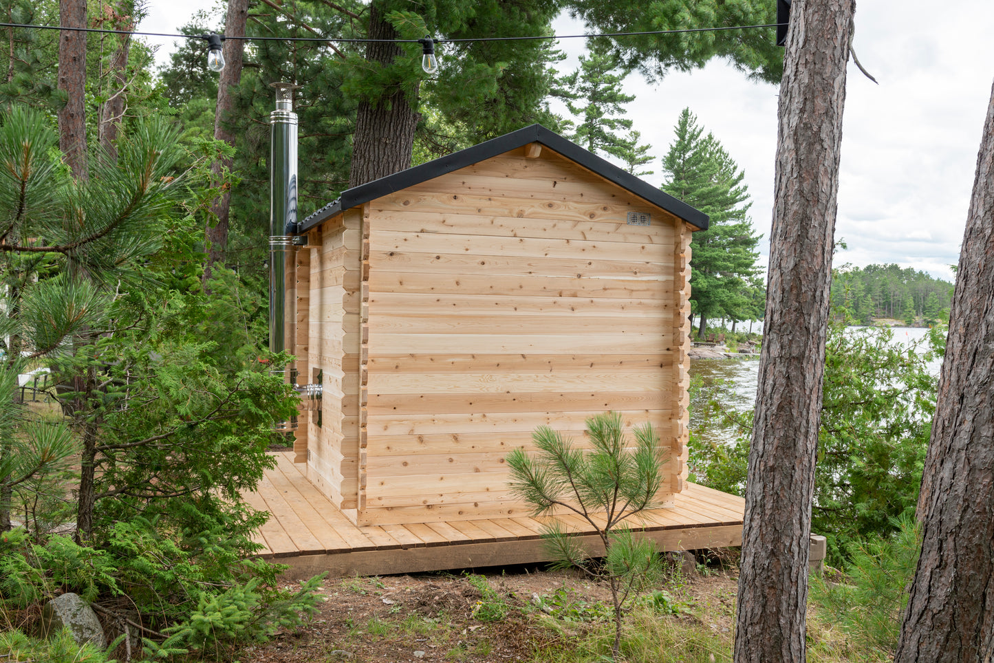 Wooden cabin in a forested area with trees and a body of water in the background