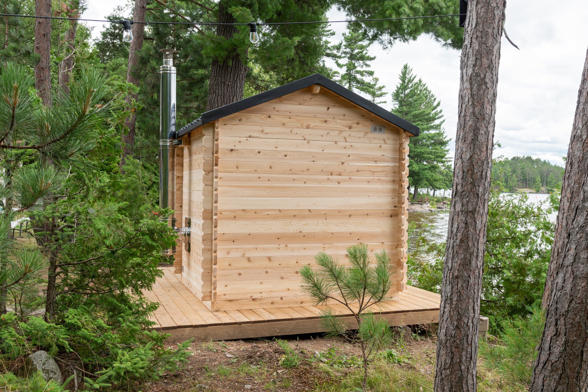 Wooden cabin in a forested area with trees and a body of water in the background