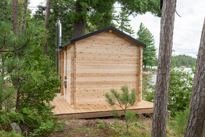 Wooden cabin in a forested area with trees and a body of water in the background