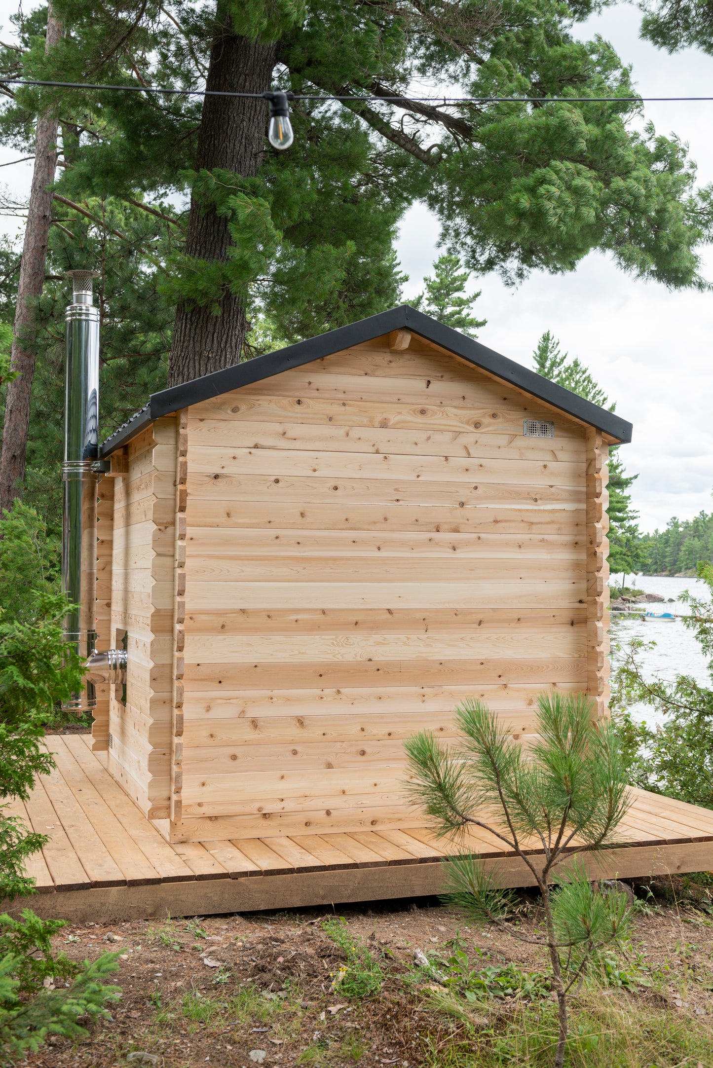 Wooden cabin in a forested area with trees and a clear sky.