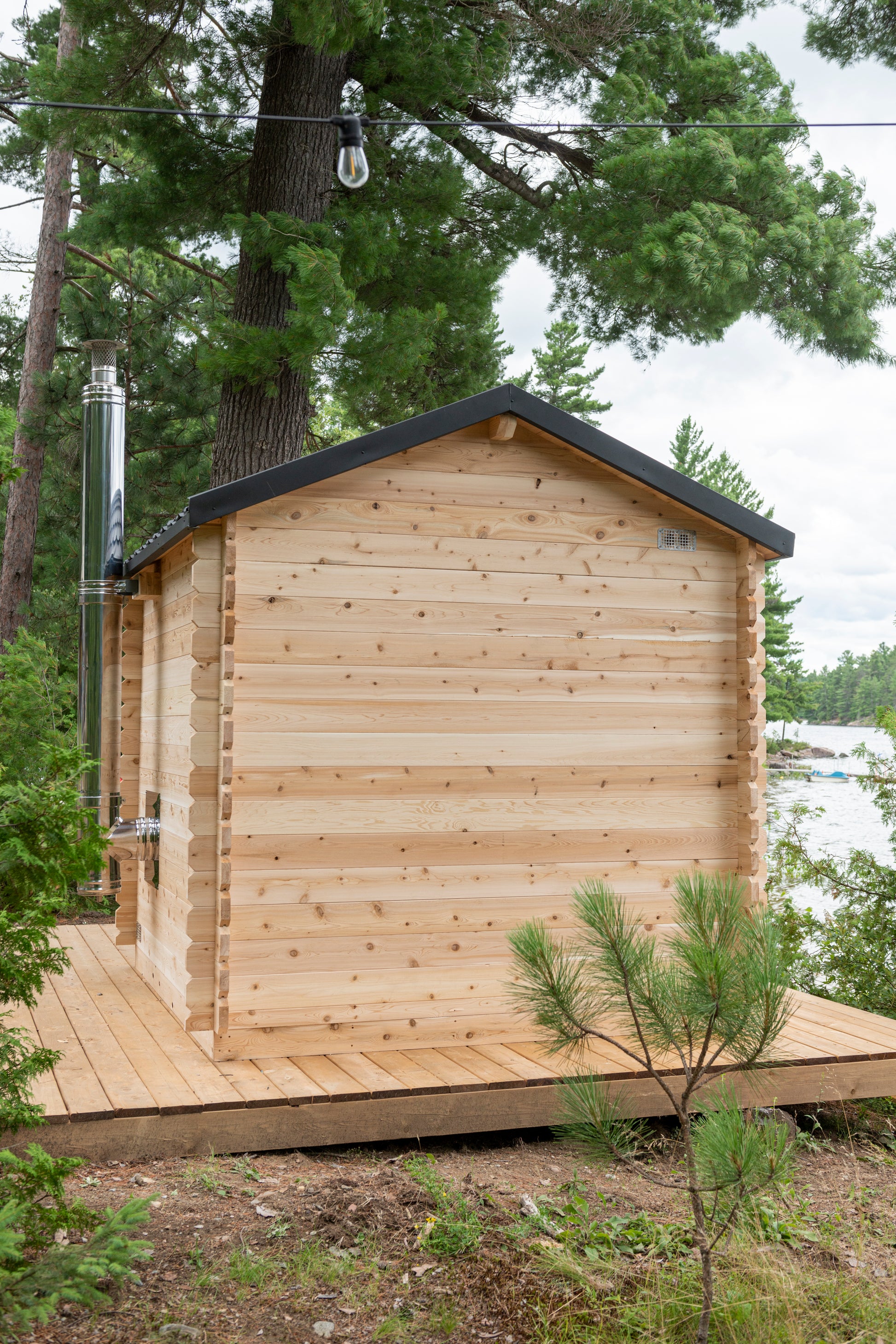 Wooden cabin in a forested area with trees and a clear sky.