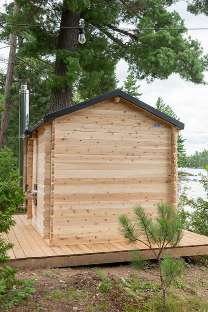 Wooden cabin in a forested area with trees and a clear sky.