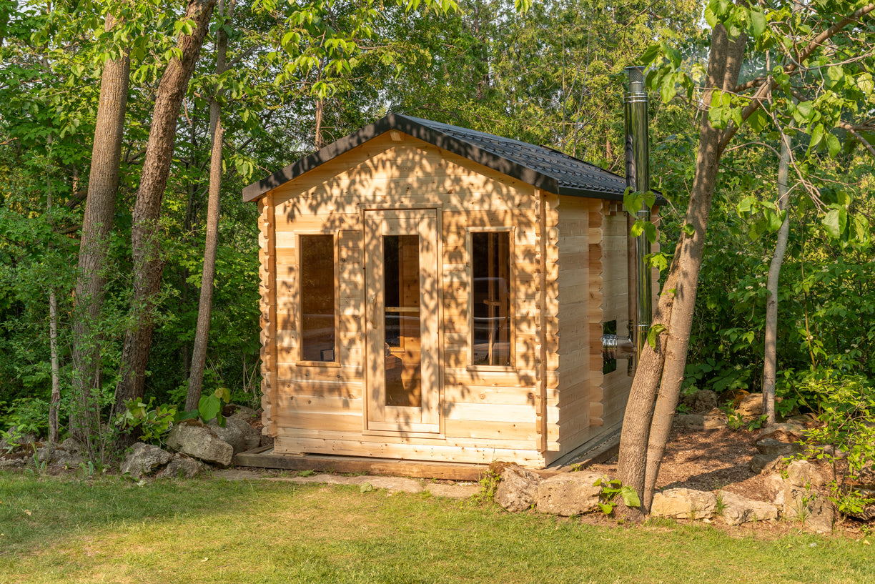 Small wooden cabin in a forest setting with trees and grass around.