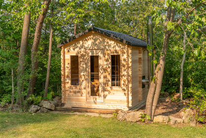 Small wooden cabin in a forest setting with trees and grass around.