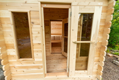 Wooden cabin with open doors, showing interior and surrounding greenery.