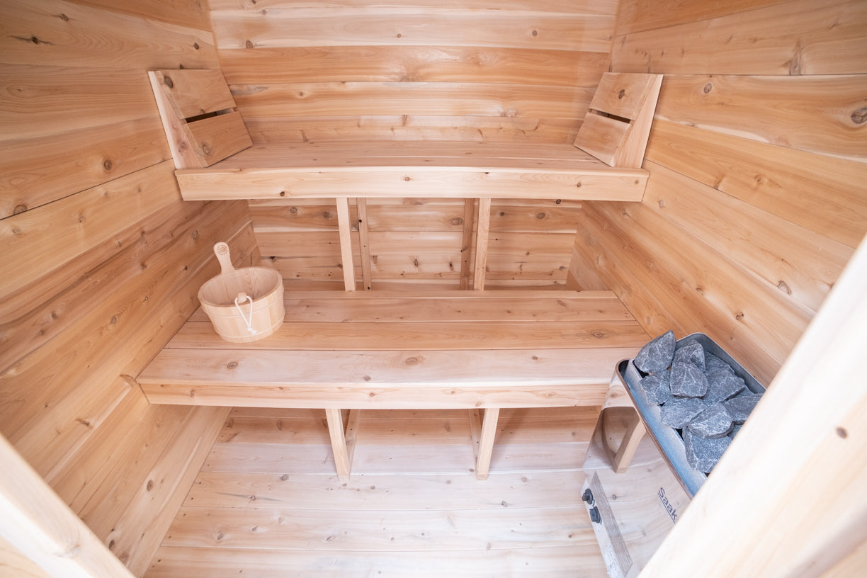 Wooden sauna interior with a bench, bucket, and stones.