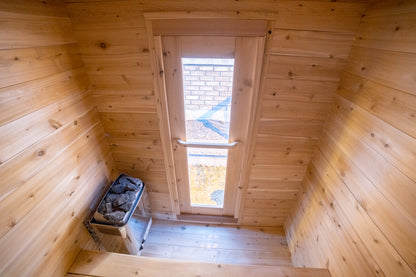 Wooden sauna interior with a window and rocks for sauna use.