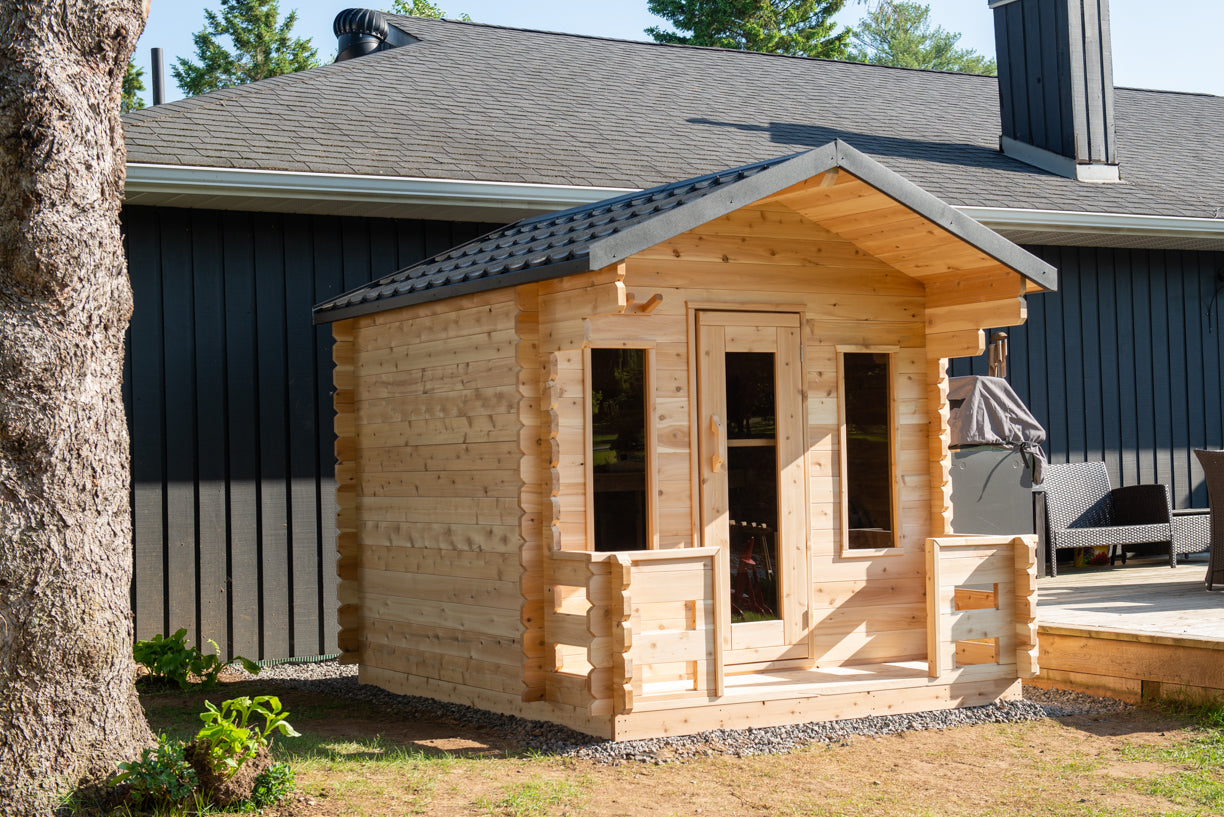 Wooden cabin attached to a house with trees in the background