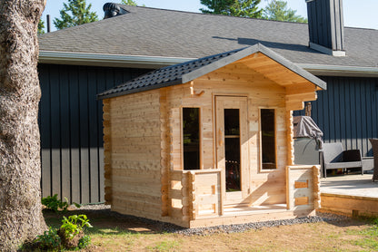 Wooden cabin attached to a house with trees in the background