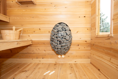 Wooden sauna interior with a basket, rocks, and a window.