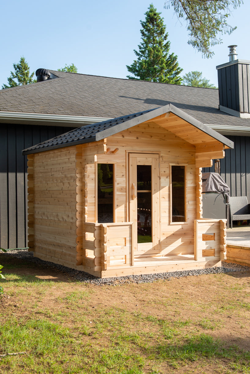 Wooden sauna cabin next to a house with trees in the background
