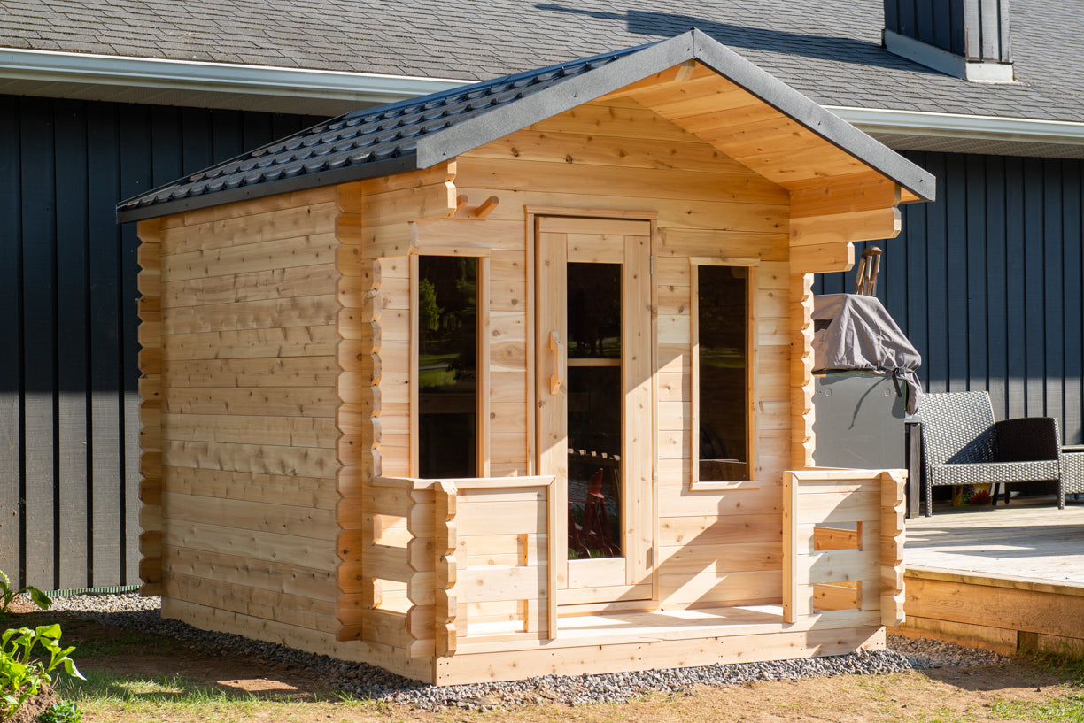 Wooden sauna with porch and a gray roof in front of a building
