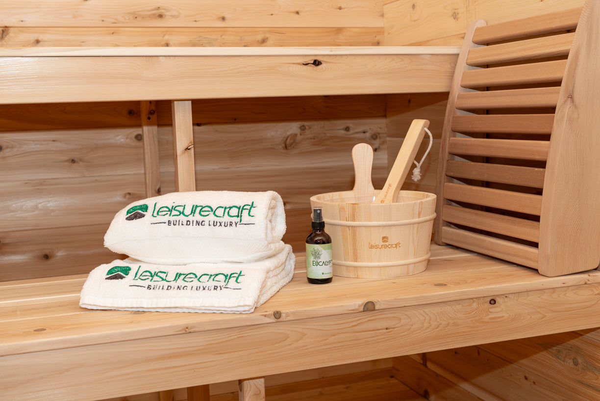 Wooden sauna bench with Leisurecraft towels, bucket, and bottle on a wooden background