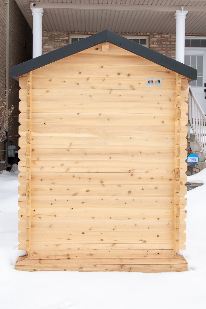 Wooden shed with a dark roof in front of a house