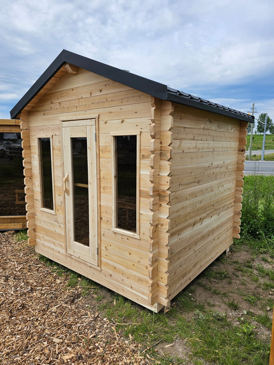 Wooden log cabin with a black roof on a grassy area with a clear sky.