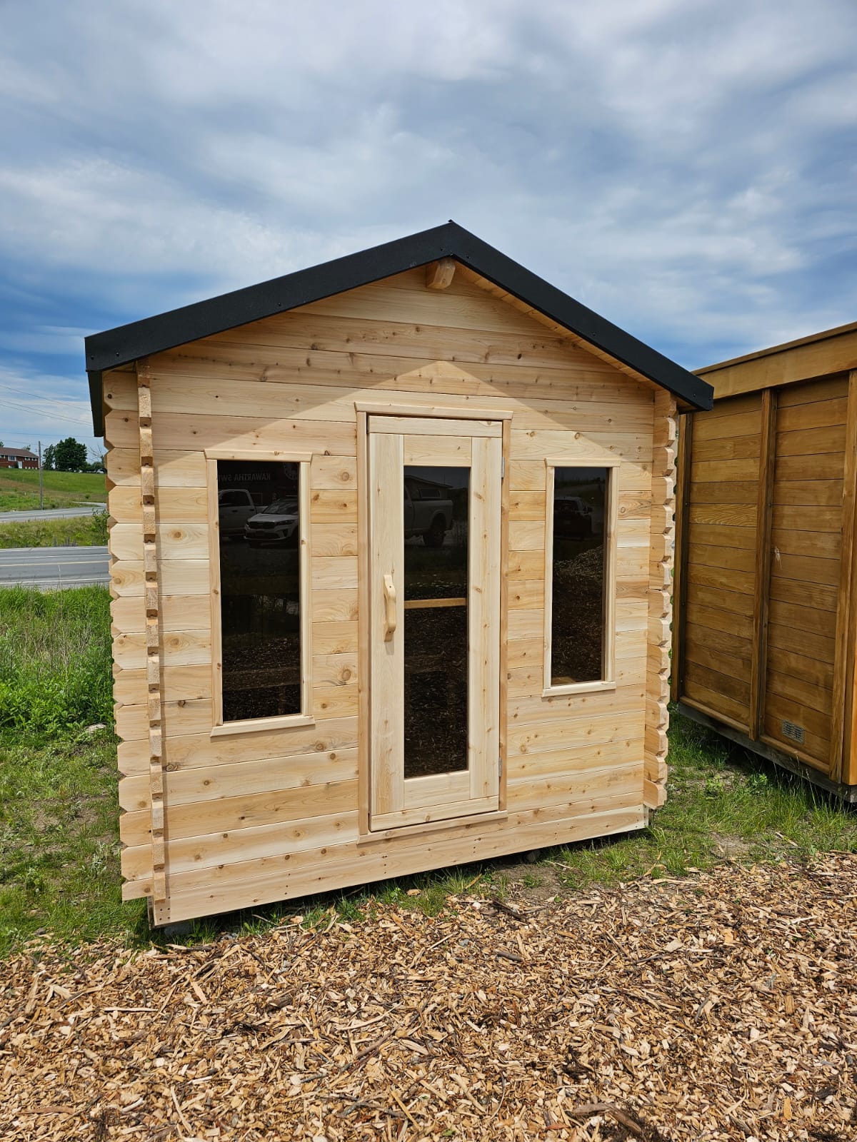 Wooden shed with a black roof on a grassy area with a clear sky.