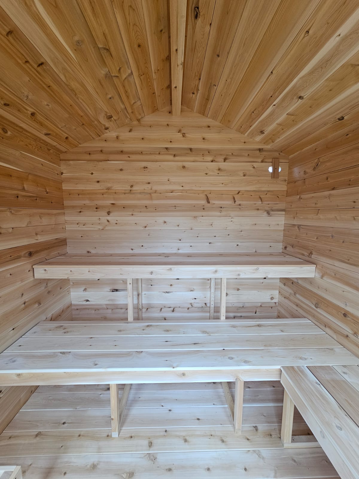 Wooden interior of a small cabin with benches and a sloping ceiling.